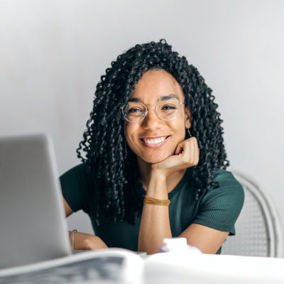 young woman sitting at table on computer smiling into camera