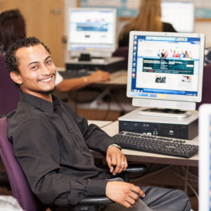 man in black button up shirt at career center computer lab faces camera smiling